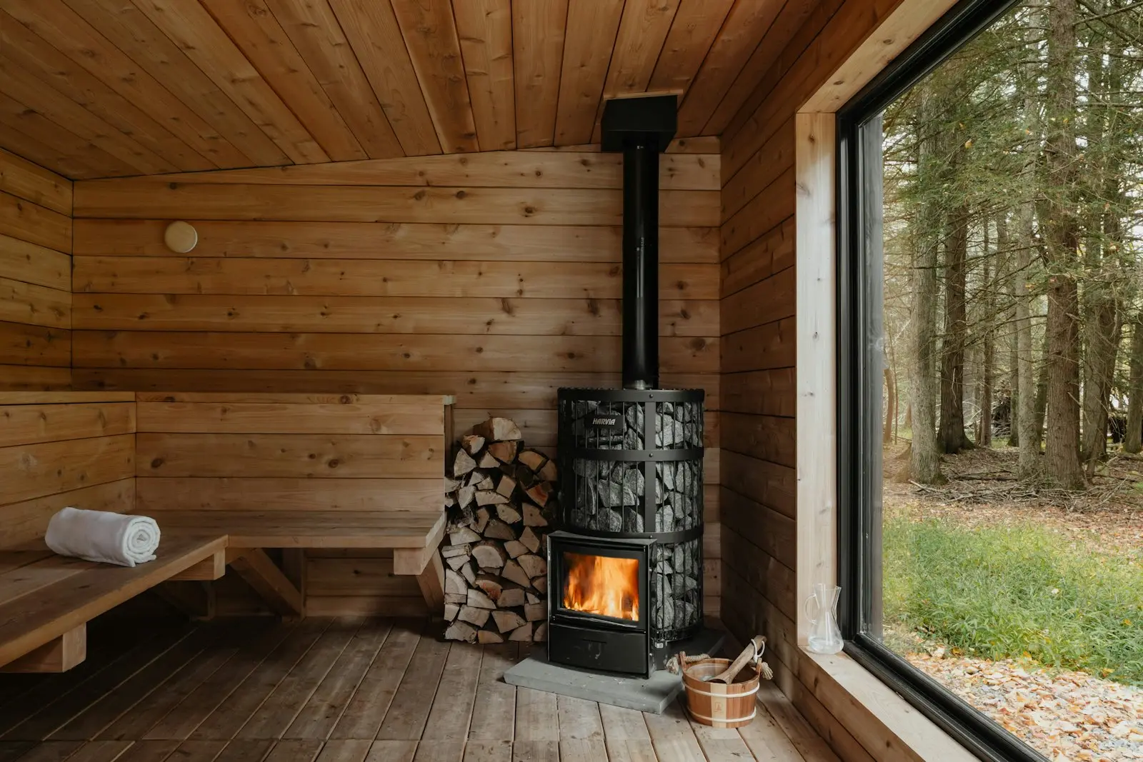 Finská sauna s kamny na dřevo a velkým oknem do lesa