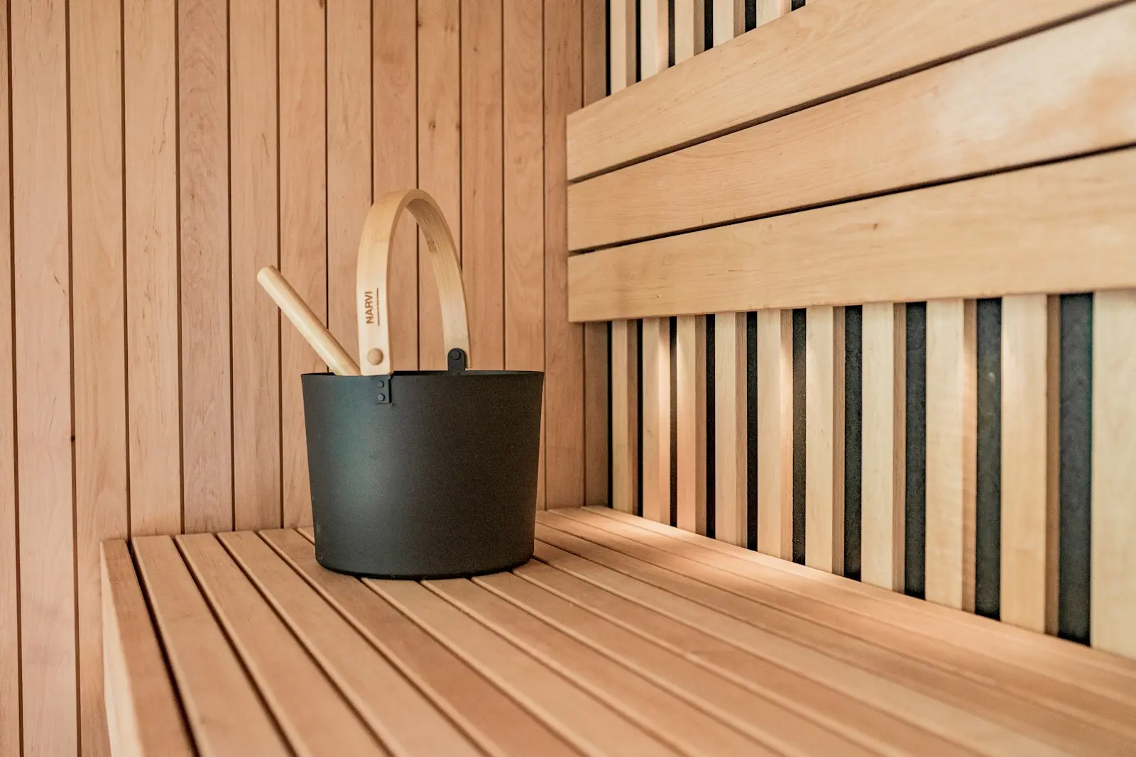 Světlá finská sauna s černým vědrem a dřevěnou naběračkou