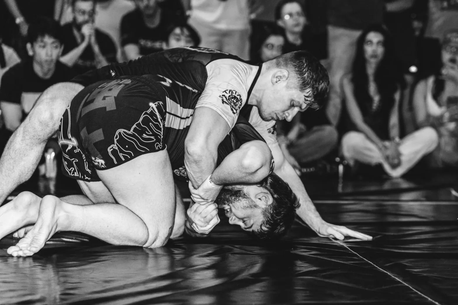Zápas v grapplingu na soutěži, diváci sedí kolem tatami