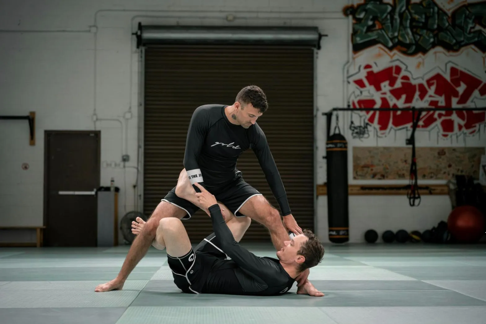 No-gi grappling: trenér v rashguardu kontroluje partnera na zemi