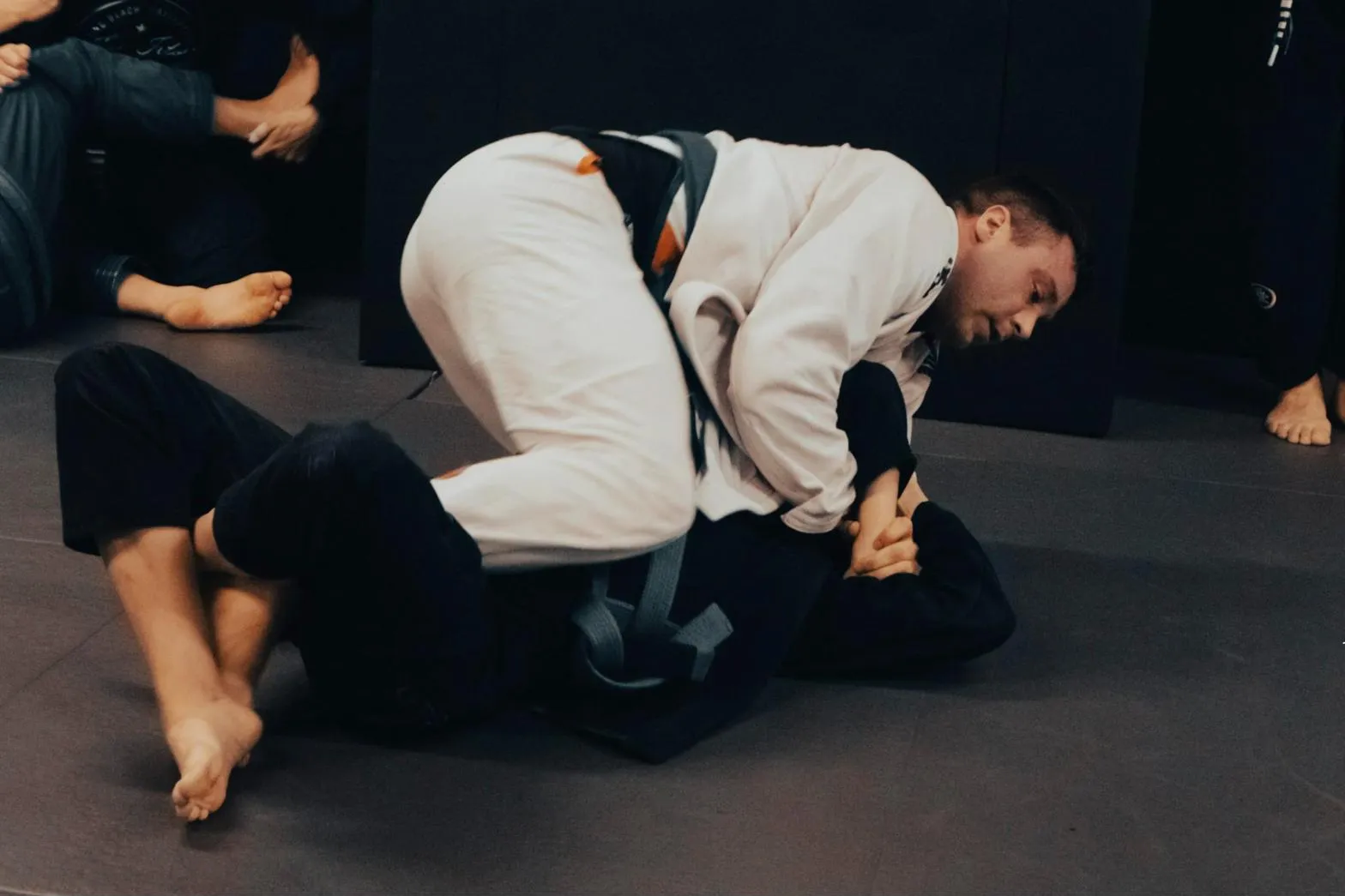 Trénink brazilského jiu-jitsu v gi: partner v bílém kimonu s modrým páskem v horní pozici