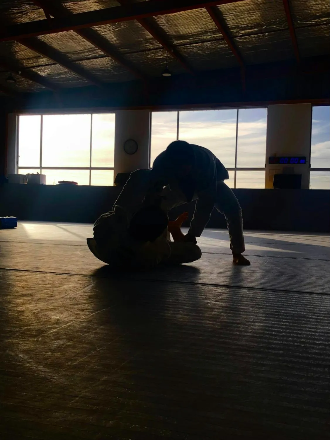 Dva zápasníci v kimonu trénují na tatami v hale s velkými okny