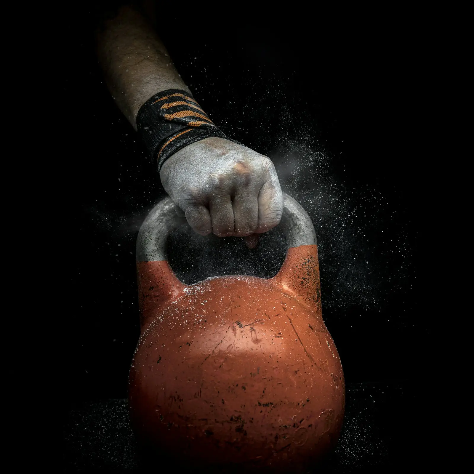 Ruka v bandáži drží kettlebell, prach z magnézia