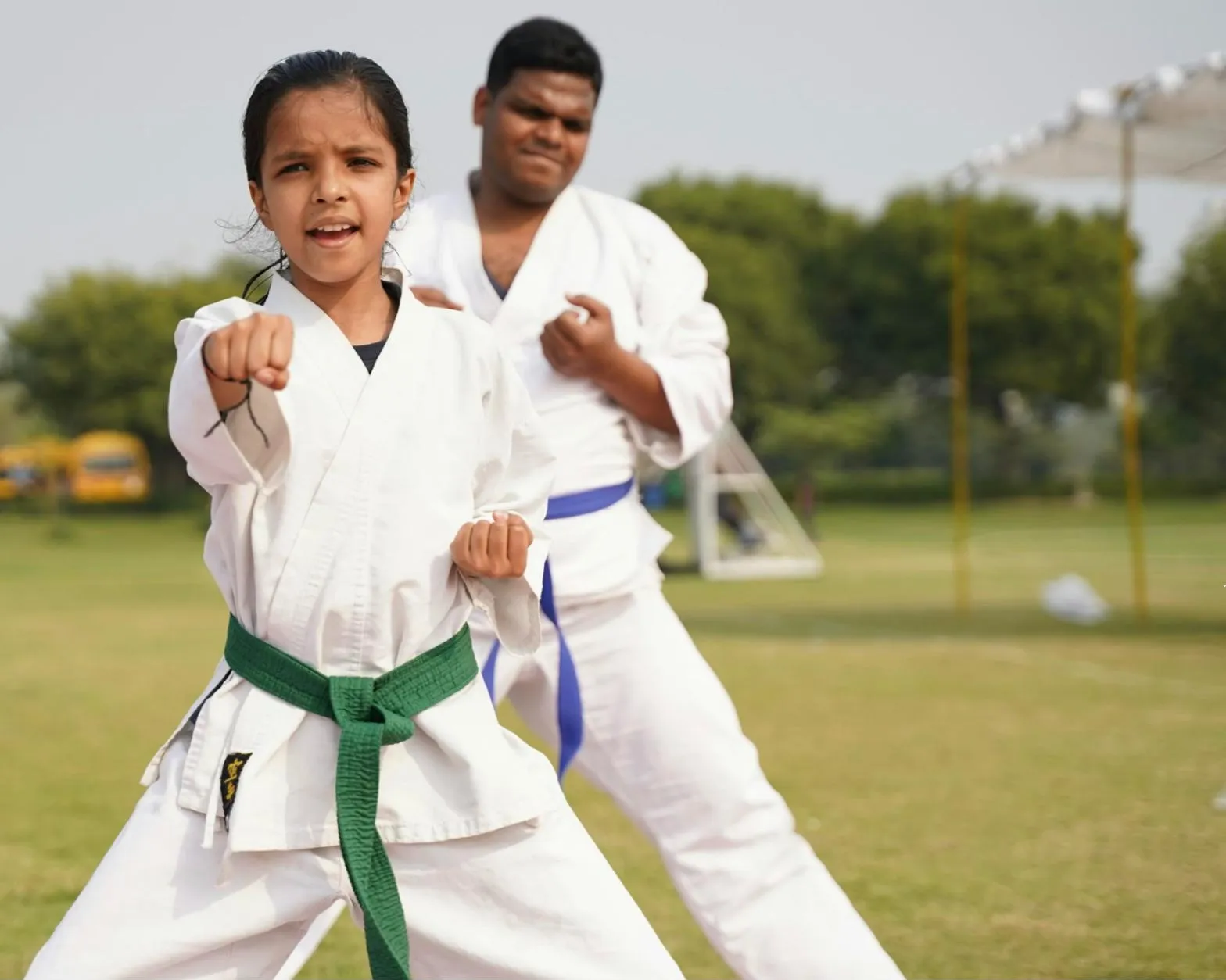 Dívka se zeleným páskem cvičí karate úder, za ní starší cvičenec